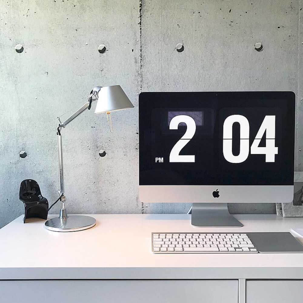 Artemide Tolomeo Micro Tischlampe neben iMac und Tastatur auf modernem Schreibtisch mit Betonwand im Hintergrund.