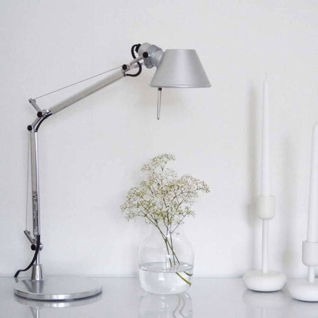 Artemide Tolomeo Micro Tischlampe in silber mit dekorativer Blume und Kerzen auf dem Tisch.