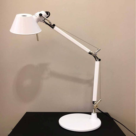Artemide Tolomeo Micro Tischlampe in Weiß mit schwenkbarem Arm auf schwarzem Tisch.