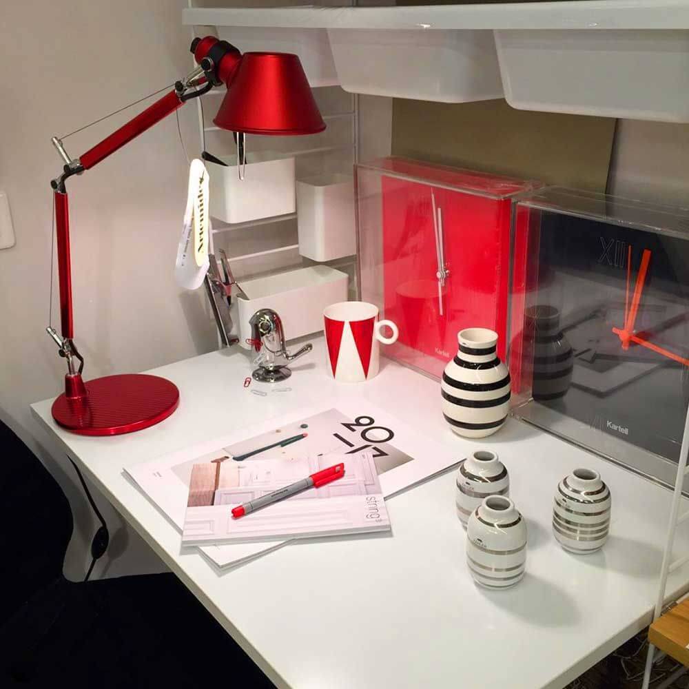 Ein rotes Artemide Tolomeo Micro Tischlampe auf einem Schreibtisch mit Deko-Elementen und Büromaterialien.