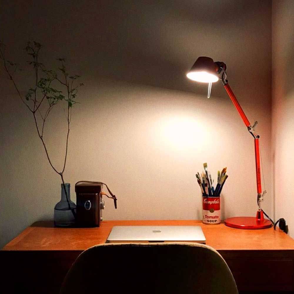 Schreibtisch mit roter Tischlampe, Laptop, Pflanzen und Stiftebehälter in einem modernen Arbeitsumfeld.