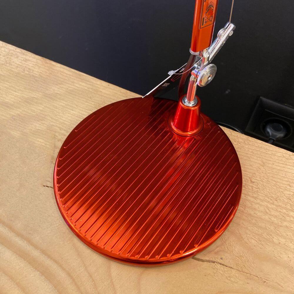 Detailaufnahme der roten Basis der Artemide Tolomeo Micro Tischlampe auf einem Holztisch.