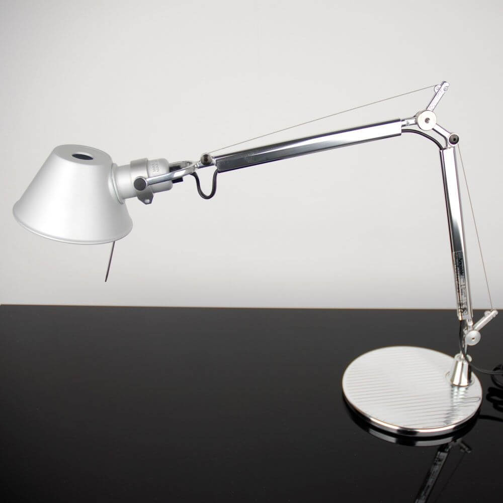 Artemide Tolomeo Micro Tischlampe in silberner Ausführung auf schwarzem Tisch mit elegantem Design.