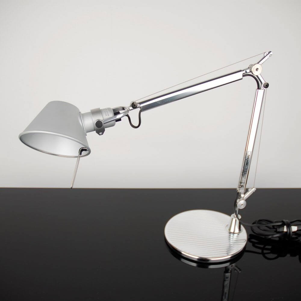Artemide Tolomeo Micro Tischlampe mit glänzender Chromoberfläche und verstellbarem Arm auf schwarzem Tisch