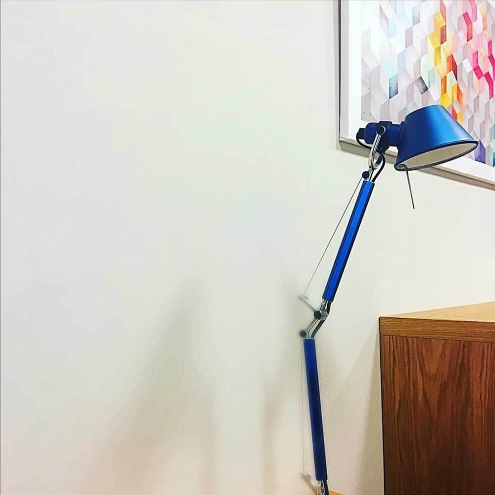 Artemide Tolomeo Micro Wandleuchte schwenkbar in Blau an einer Wand mit Kunstwerk.