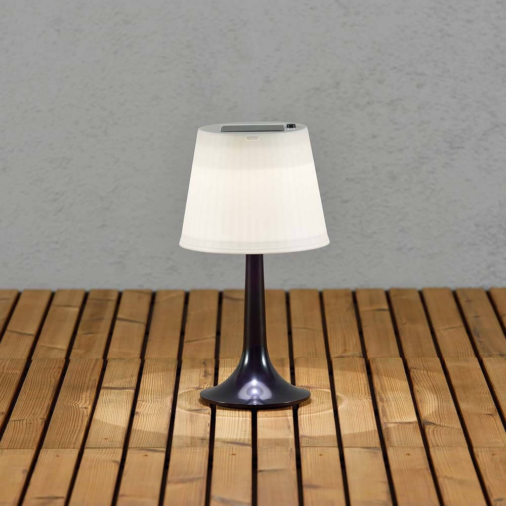 LED Tischlampe Assisi Schwarz auf Holztisch mit solarbetriebenem Lampenschirm.