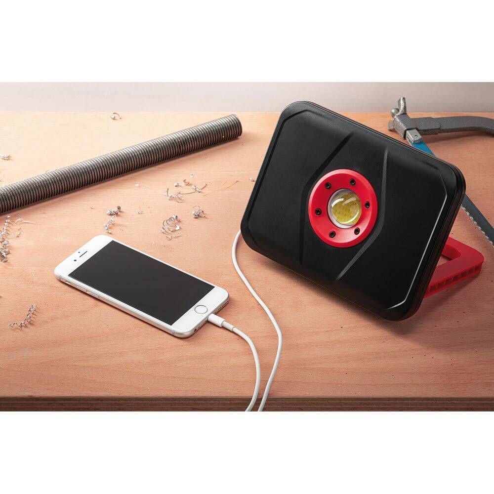 LED Akkuleuchte Worklight in Schwarz und Rot, USB-Ladefunktion, Powerbank-Funktion, auf Holzunterlage mit Smartphone.