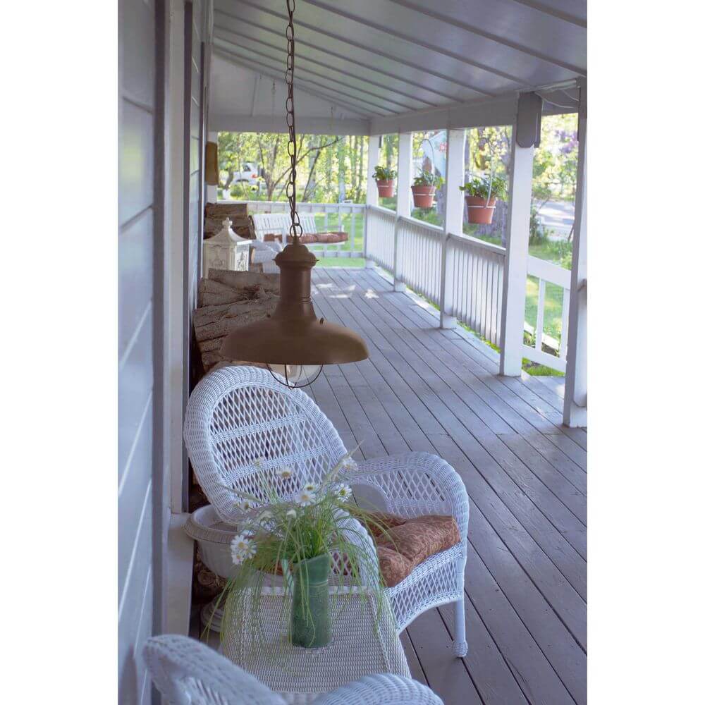 Außen-Hängelampe ESTORIL-G IP33 Rostbraun hängt über einem gemütlichen Sitzbereich auf der Veranda.