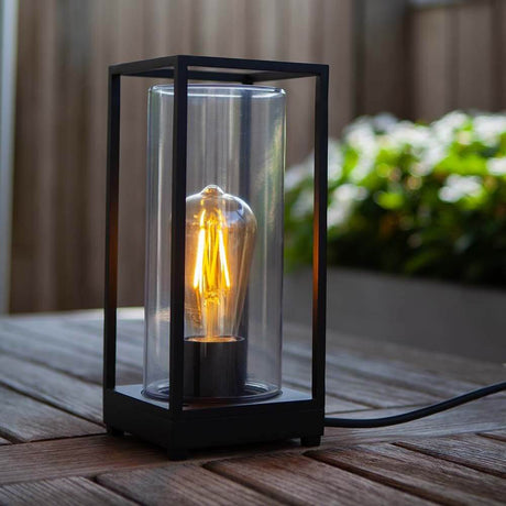 Außentischleuchte Flair mit Glaszylinder auf einem Holztisch mit romantischem Licht.