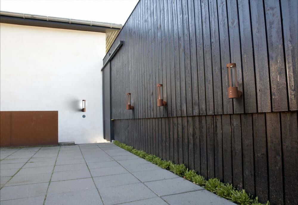 Außenwandlampe Helix IP44 an einer modernen Holzwand, die indirektes Licht abgibt.
