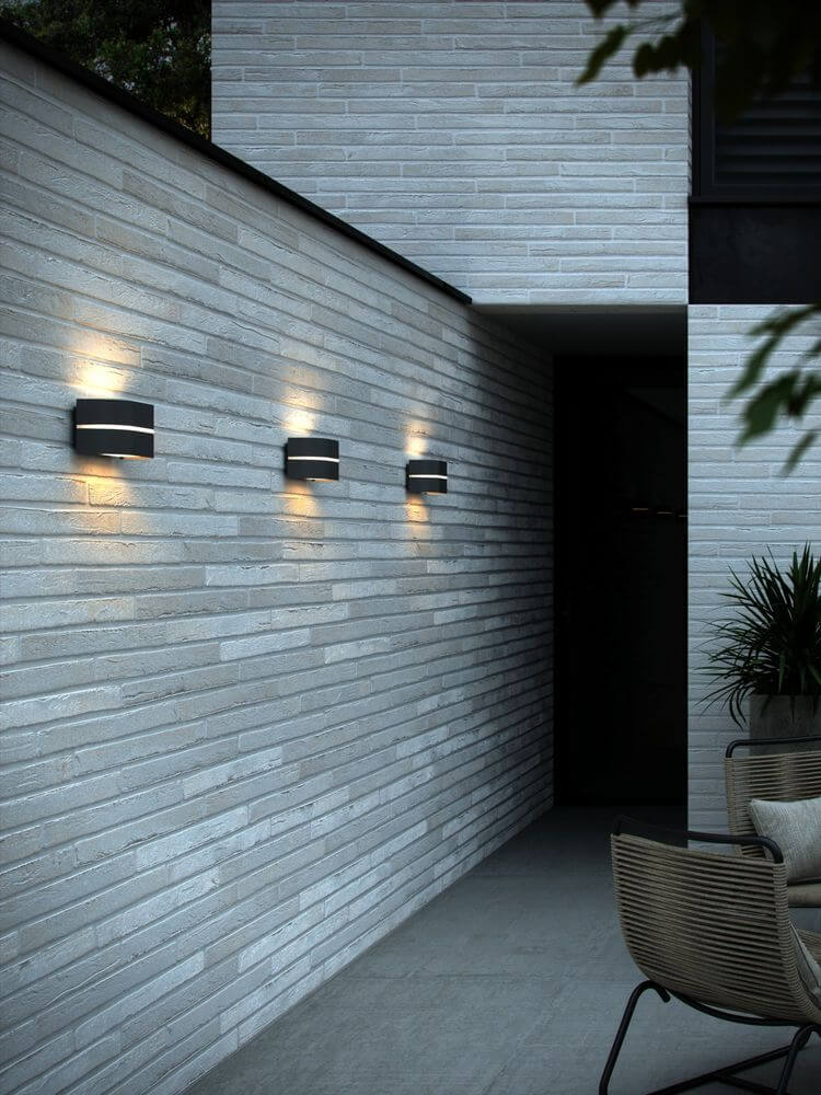 Außenwandlampe Sibelis IP44 an moderne Wand, strahlt sanftes Licht auf helle Fassade.