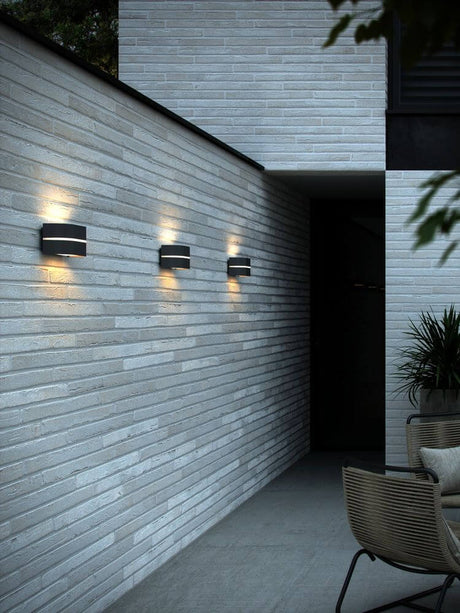 Utendørs vegglampe Sibelis IP44 på moderne vegg, avgir mykt lys på lys fasade.
