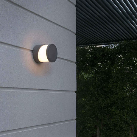 Außenwandleuchte BLOCK IP65 Zementgrau an Wand mit warmem Licht, ideal für Garten und Terrasse.