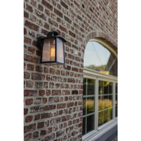 Applique murale extérieure Kelsey IP44 noire installée sur un mur en briques, idéale pour le jardin et les allées.