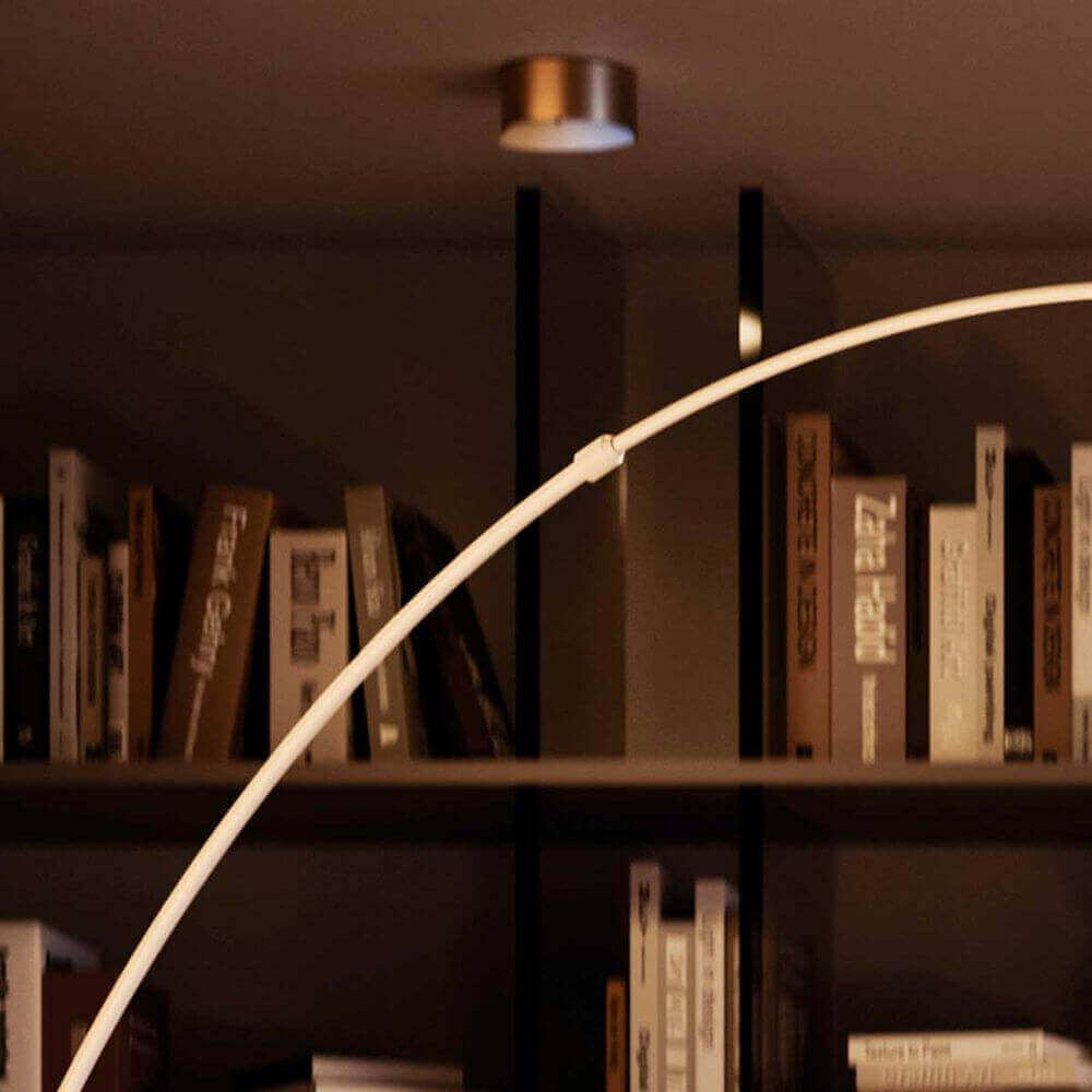 Moderne Stehlampe im Wohnzimmer vor einer Bücherwand, warmes Licht und gemütliche Atmosphäre.
