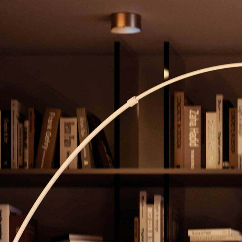 Moderne Stehlampe im Wohnzimmer vor einer Bücherwand, warmes Licht und gemütliche Atmosphäre.