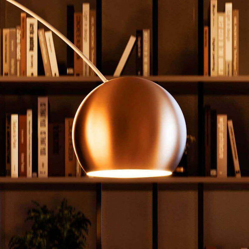 Moderna Stehlampe mit goldener Kugel und warmem Licht vor Bücherregal in stilvollem Raum.