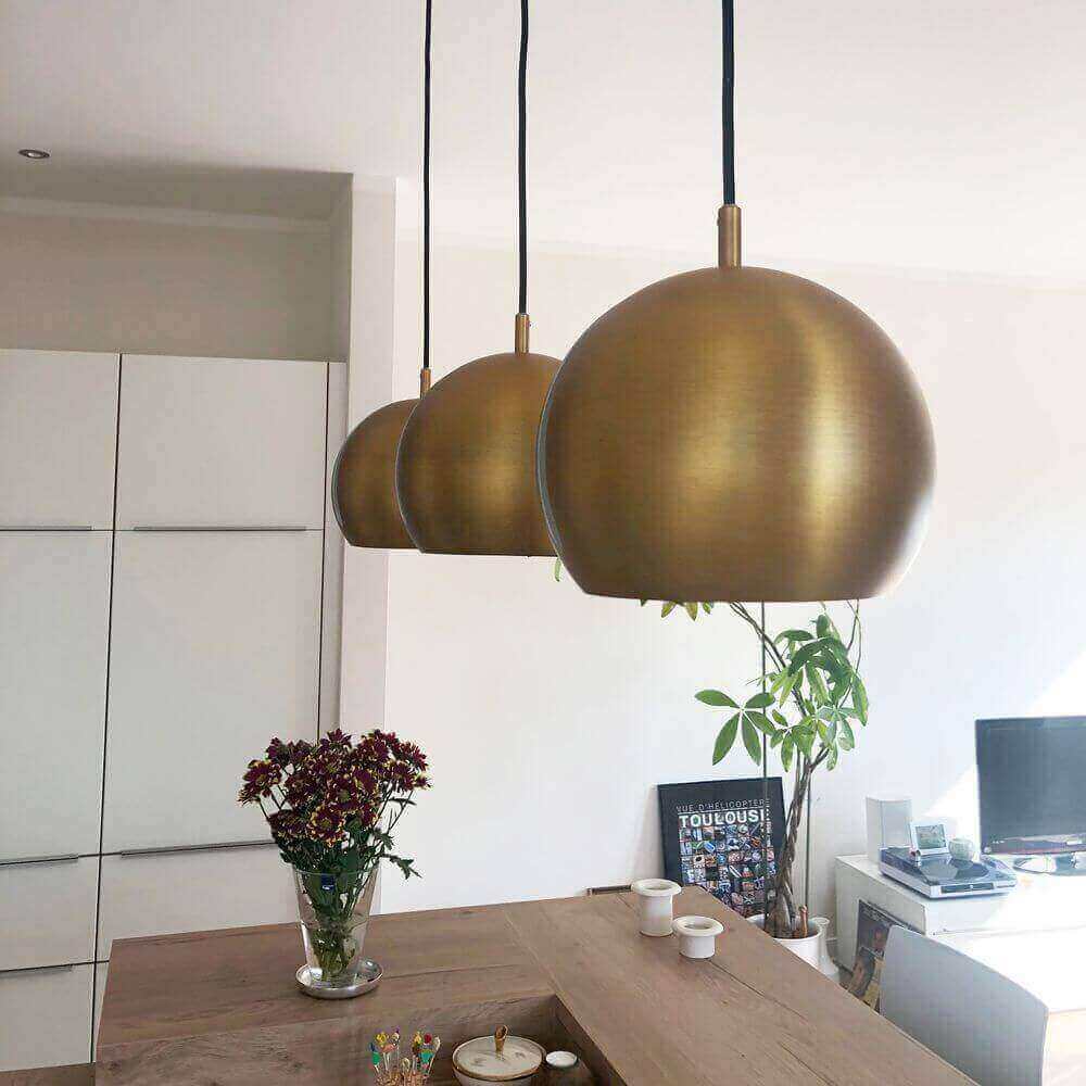 Moderne goldene Pendelleuchten hängen über einem hellen Küchentisch mit Pflanzen und dekorativen Elementen.