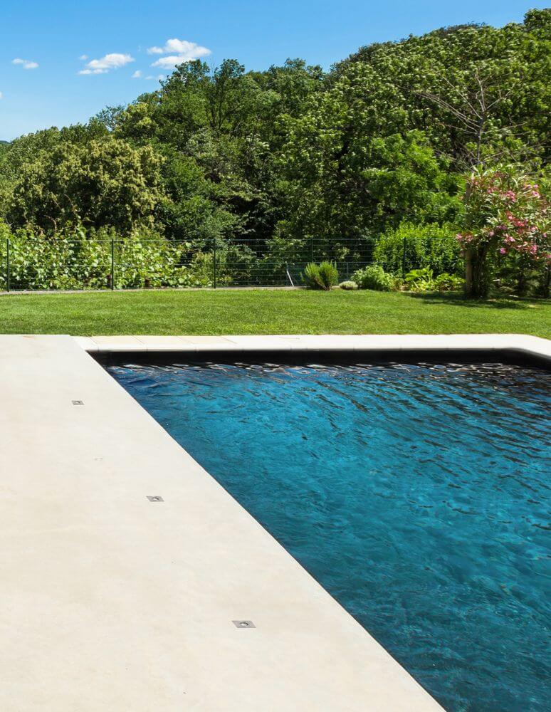 Bang LED Außenbodeneinbauleuchte Nickel IP67 neben einem modernen Pool in einer grünen Umgebung.
