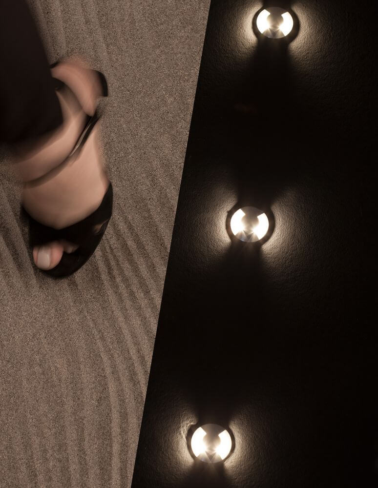 Bang LED Außenbodeneinbauleuchte Nickel IP67 in einer modernen Umgebung mit feinem Sand.