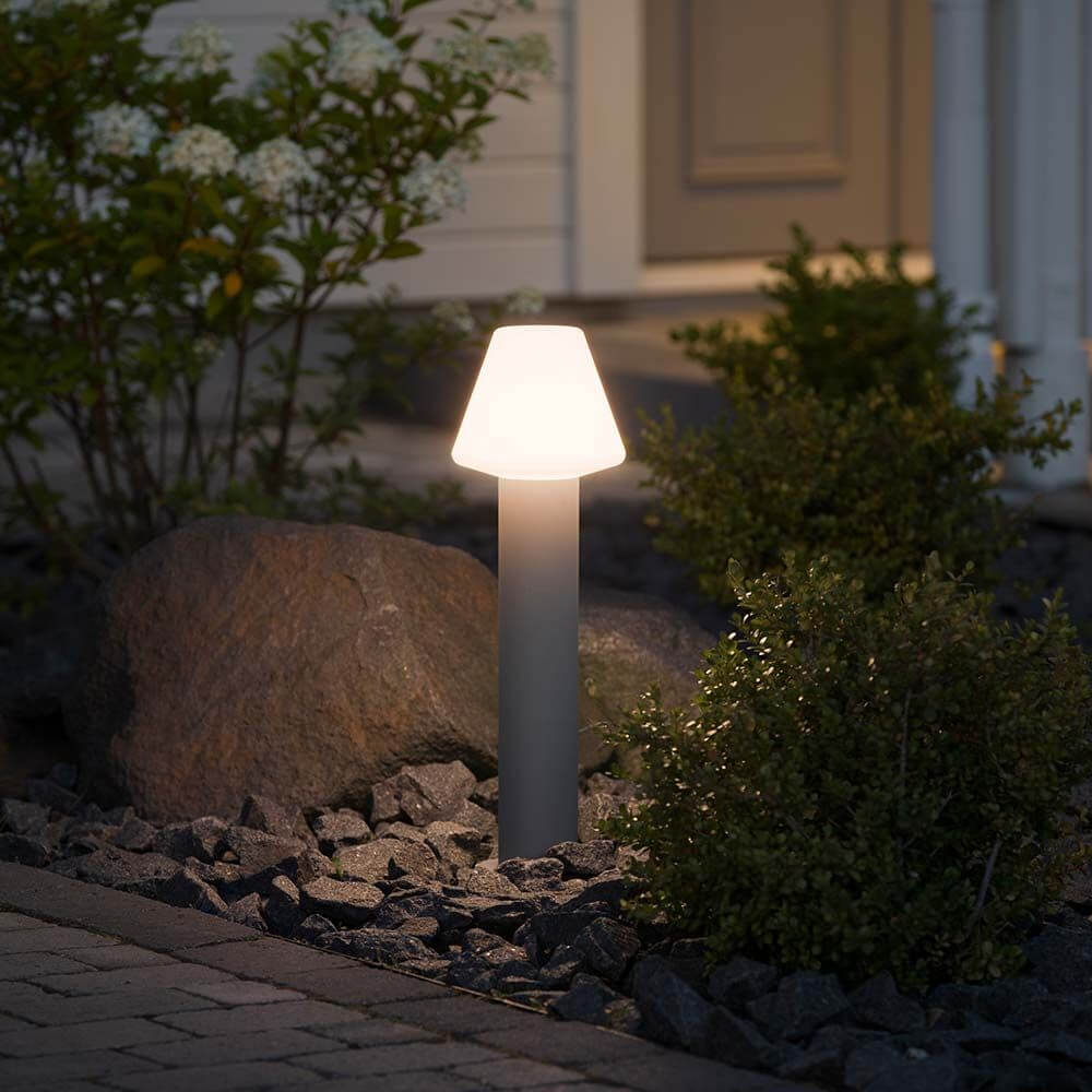 Barletta Energiespar Sockelleuchte Grau, Acrylglas im Garten, leuchtet sanft zwischen Steinen und Pflanzen.