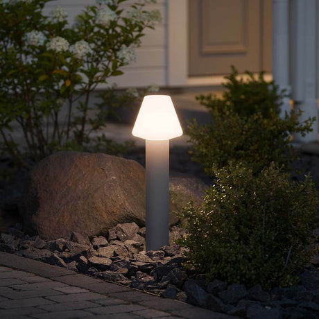 Barletta energisparande sockellampa grå, akrylglas i trädgården, lyser mjukt mellan stenar och växter.