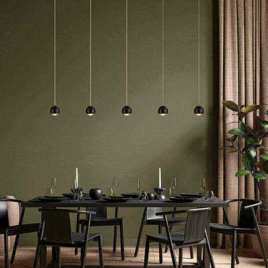 Elegantes Esszimmer mit modernen hängenden Lampen, schwarzem Tisch und Stühlen, stilvolles grün als Hintergrund.