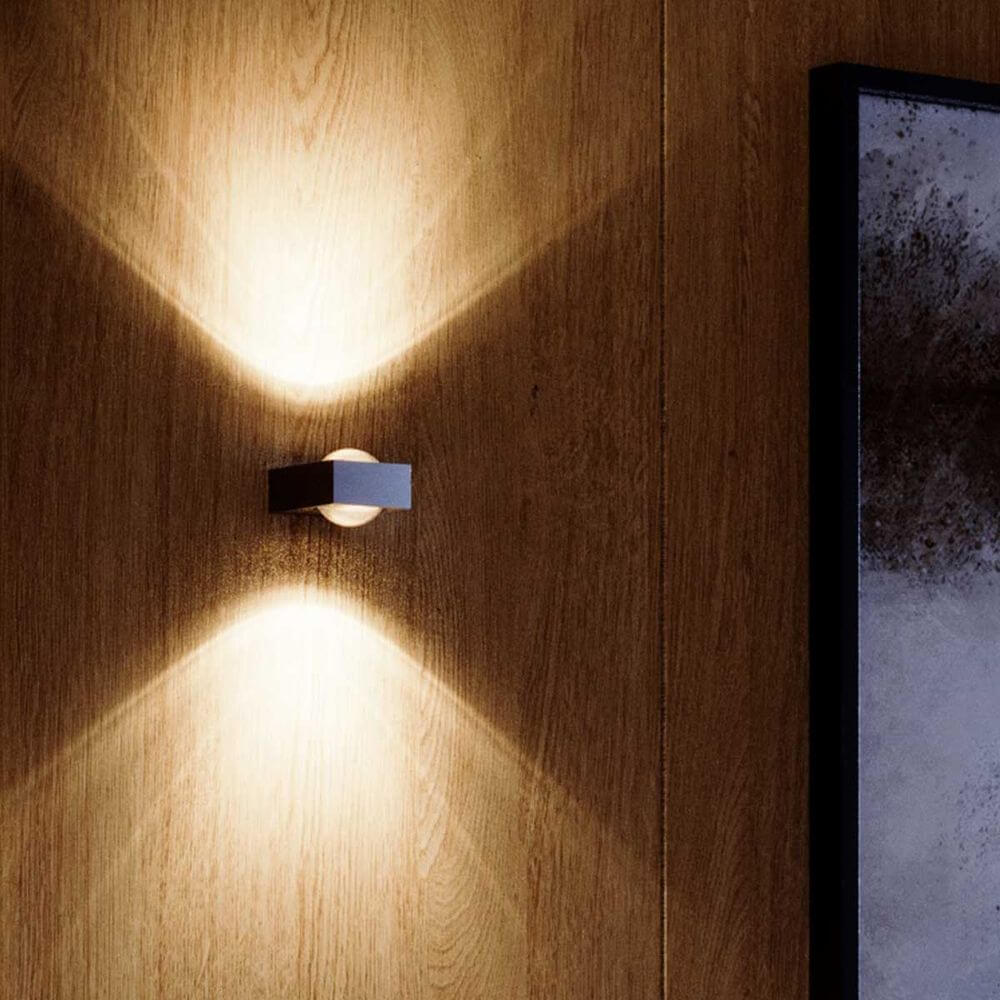 s.luce Beam X moderne Wandleuchte Up & Down eckig an einer Holzwand, erzeugt charakteristische Lichtkegel.