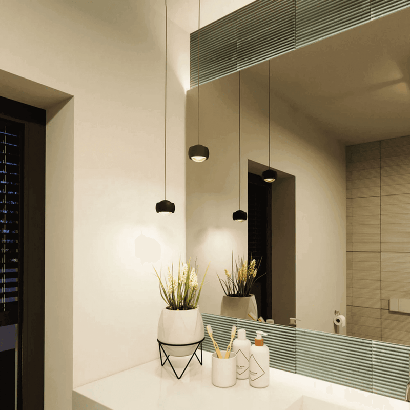 Moderne Badezimmerbeleuchtung mit minimalistischen Hängeleuchten und einem klaren Spiegel.