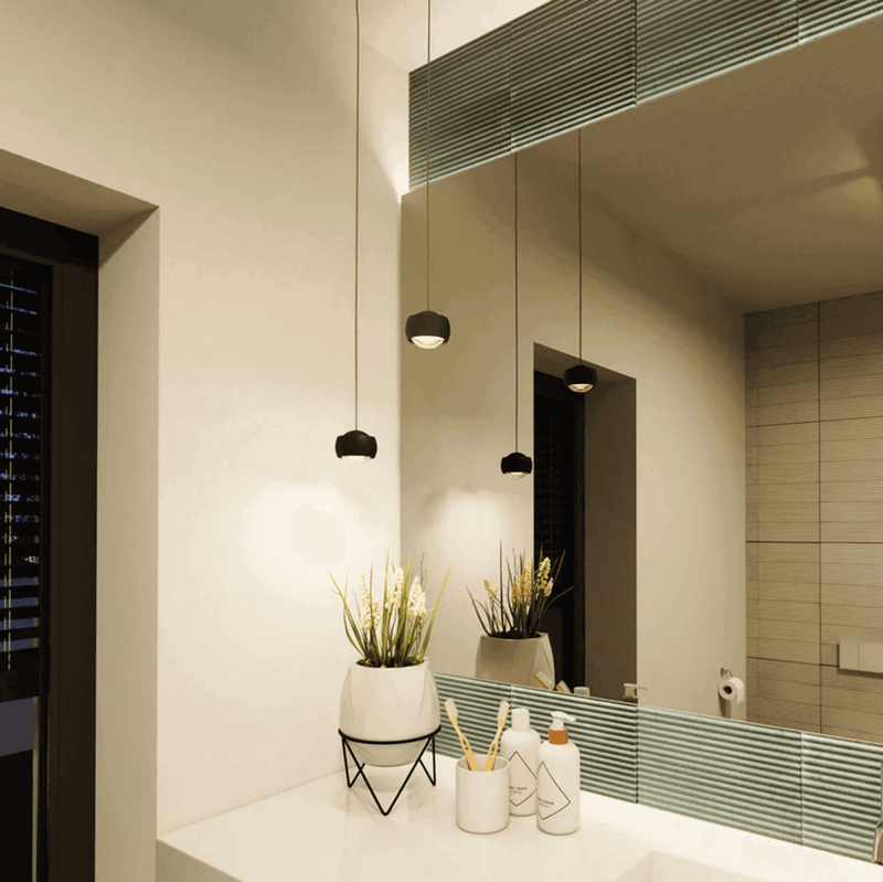 Moderne Badezimmerbeleuchtung mit minimalistischen Hängeleuchten und einem klaren Spiegel.