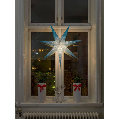 Étoile en papier bleue perforée et brodée de bleu, à 7 pointes, sans source lumineuse, éclairée à la fenêtre avec des plantes.