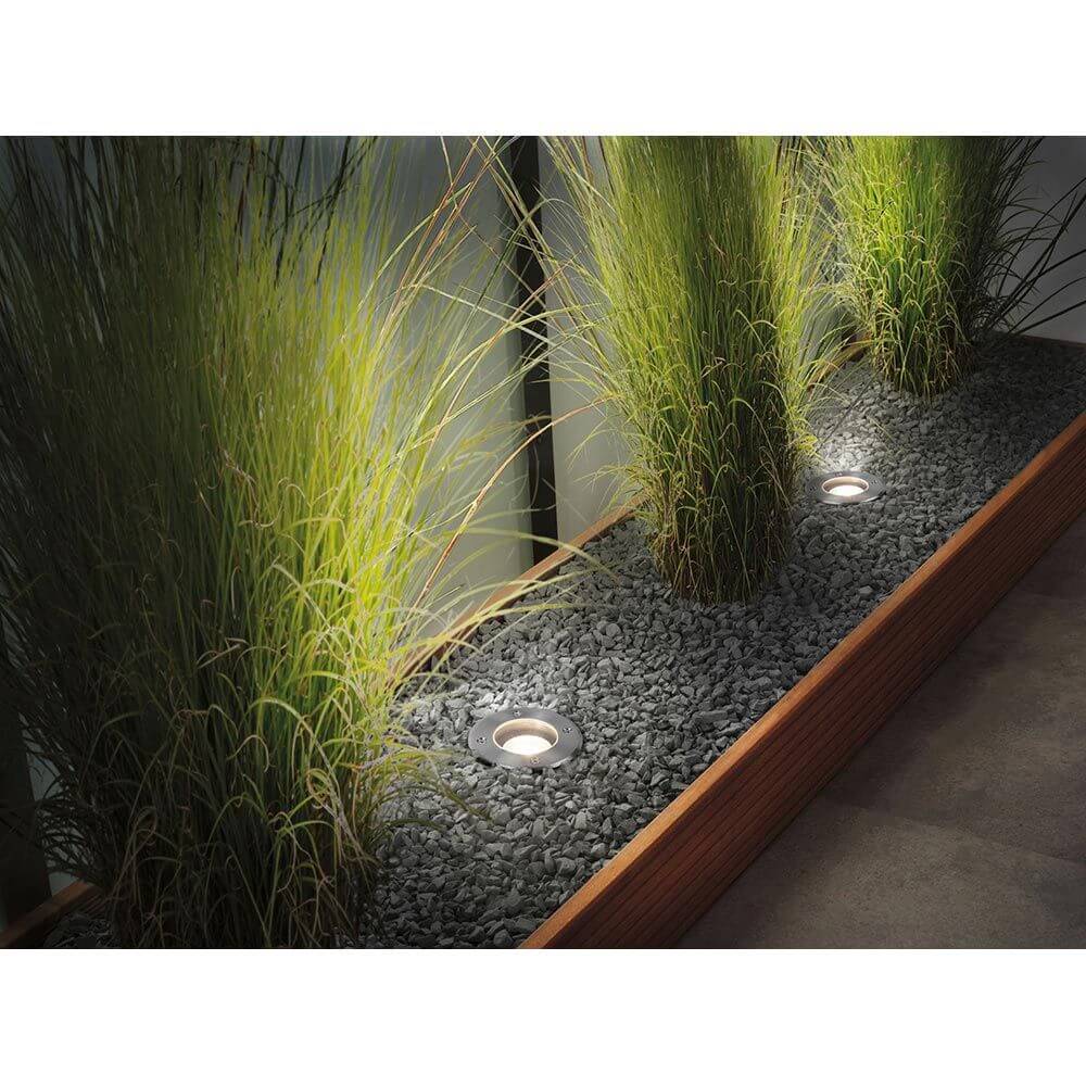 Bodeneinbauleuchte Floor 11cm Metall IP65 in einem Gartenbeet mit Gräsern und Kies.
