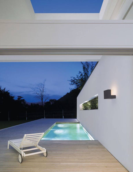Applique extérieure Brin LED 3000K Anthracite IP65 sur une façade moderne la nuit, entourée d’une piscine.