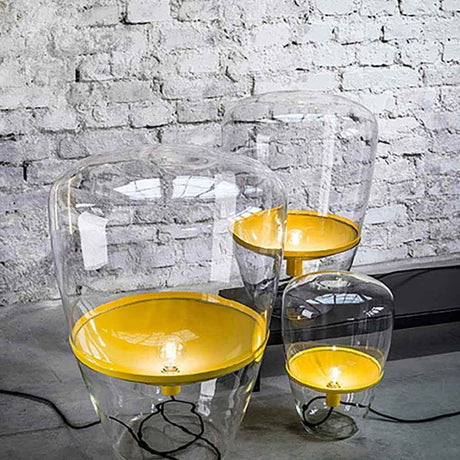 Brokis Stehleuchte Balloons Large in Glas mit gelbem Metallreflektor auf Ziegelwand.