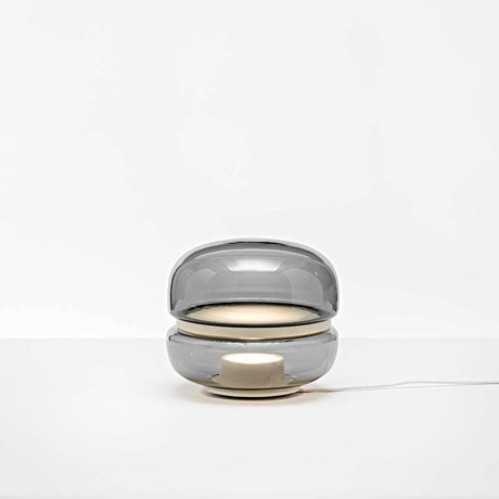 Brokis Tischlampe Macaron S mit grauem mundgeblasenem Glas und Onyxbasis, die ein sanftes Licht ausstrahlt.