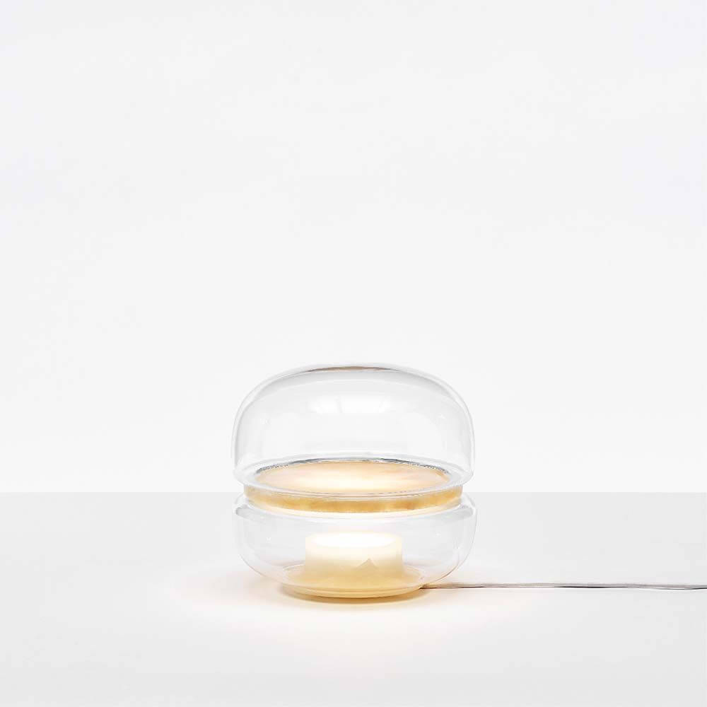 Brokis Tischlampe Macaron S mit transparentem Glas und Onyxbasis, sanftes Licht strahlt nach oben.