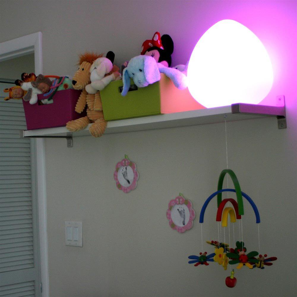 Bruchfeste LED-Akkulampe Stone in Form eines Eies mit buntem Licht über Spielzeugen auf einem Regal.