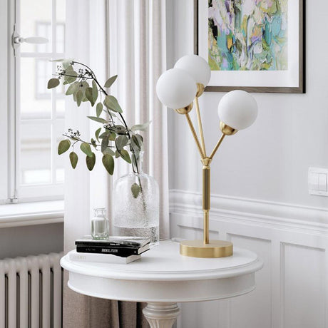 Table lamp 3Some 3-light Antique Gold on a table, surrounded by plants and artworks.
