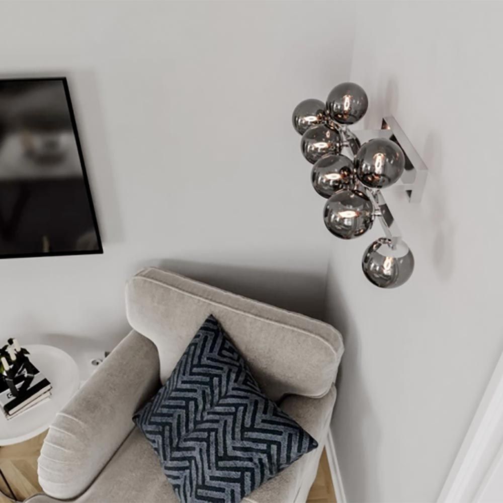 Vegg- og taklampe Splendor 9-flg krom røykglass på en vegg over en sofa.