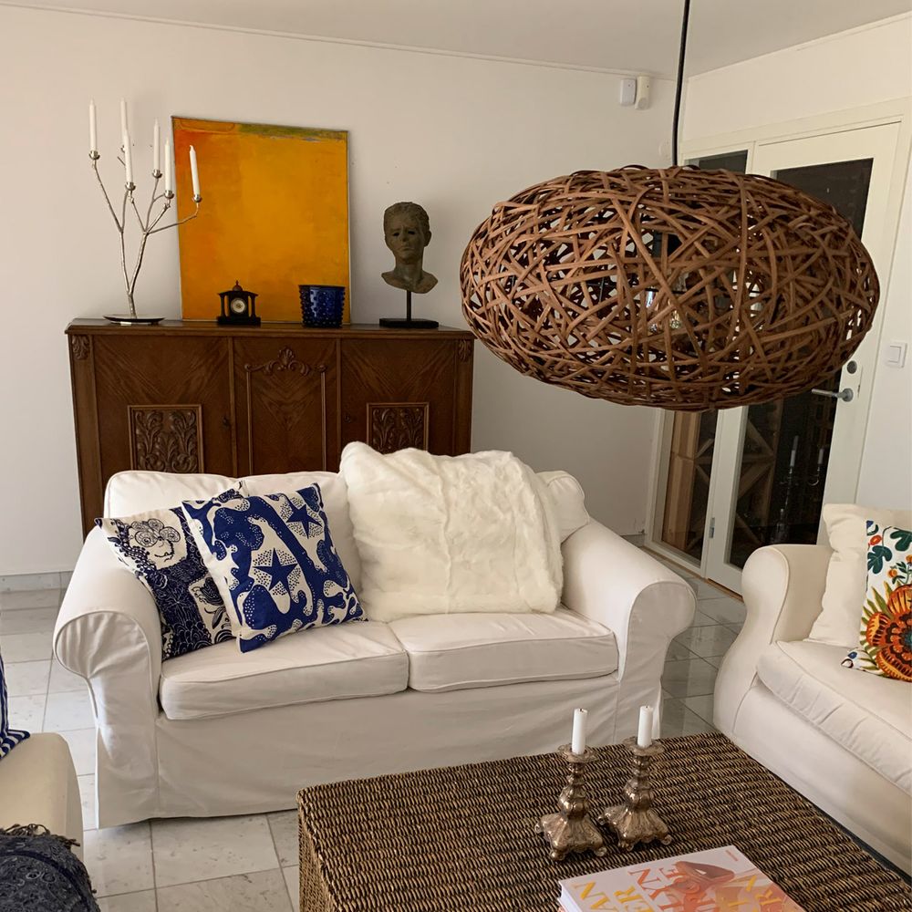 Hängeleuchte Diego aus Rattan über einem weißen Sofa im rustikalen Wohnzimmer.