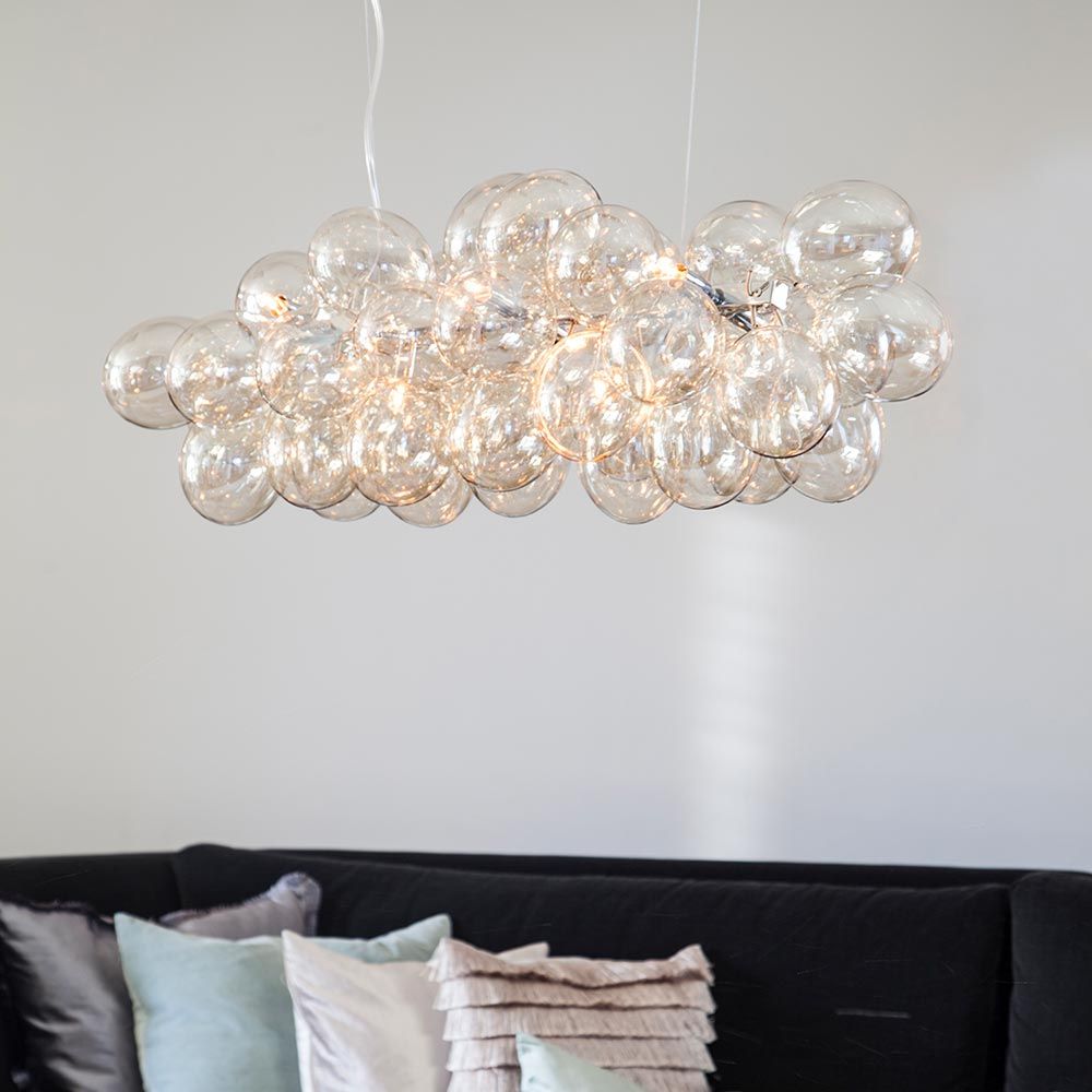 Lampada a sospensione in vetro Gross Bar 80cm con 38 palline di vetro sopra un divano in un interno moderno.