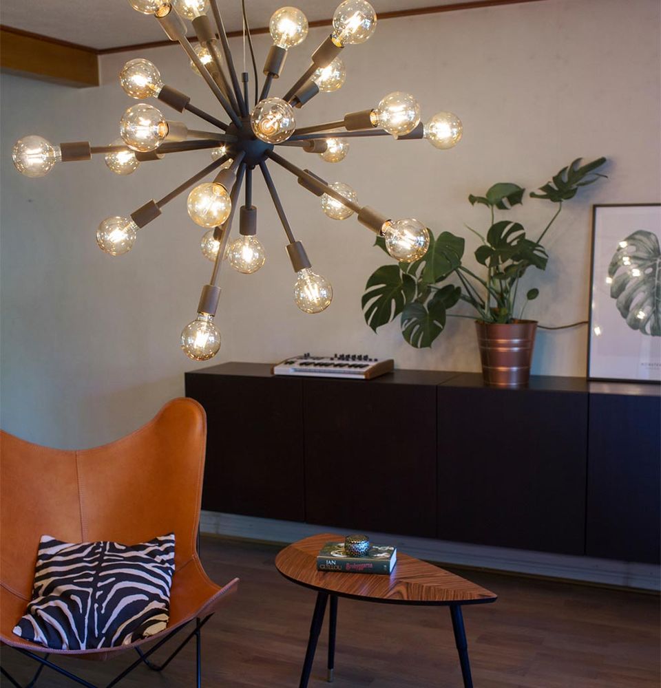 Hengelampe Leo med 24 lamper i et moderne oppholdsrom med lenestol og planter i bakgrunnen.