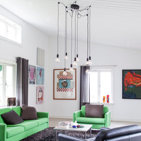 Suspension Spindelon à 9 lumières, noire, dans un espace de vie moderne avec des canapés verts et des œuvres d’art