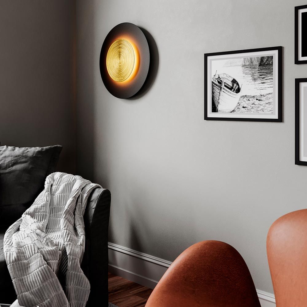 LED-vegglampe Nitra Ø 50 cm svart, gullfarget på en vegg i stuen, elegant design med varmhvitt lys.