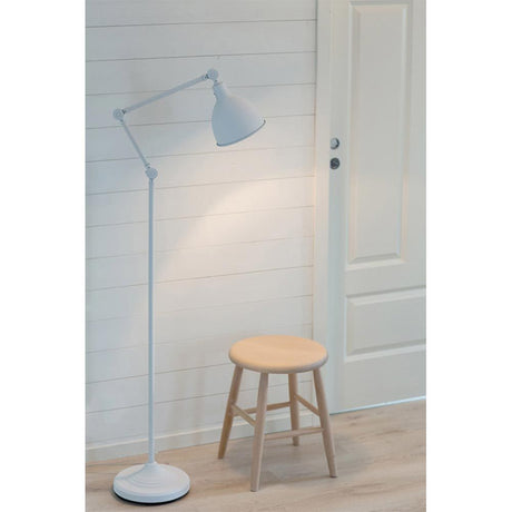 Floor lamp Bazar adjustable sand white shade next to a wooden stool in a bright room.