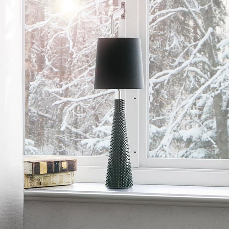 Lampe de table Lofty Slim 54cm Noir sur un rebord de fenêtre avec vue sur des arbres enneigés.