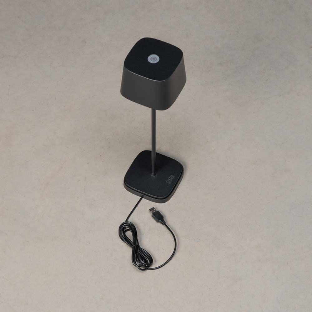 Capri USB-Tischleuchte IP54 in Schwarz mit USB-Kabel und dimmbarer Lichtstärke auf beige Hintergrund.