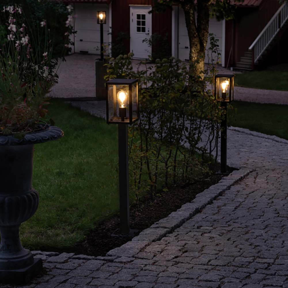 Carip Pollerleuchte Schwarz im Garten, stilvoll beleuchtet auf einem Weg, aus Stahl und klarem Glas.