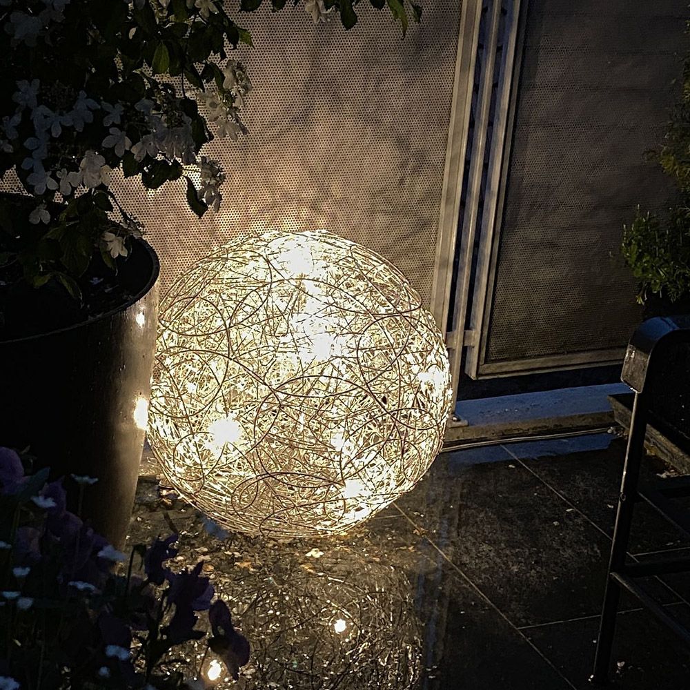 Catellani & Smith Fil de Fer F LED Außen-Drahtkugel Bodenleuchte IP65 leuchtet in einem Garten bei Nacht.