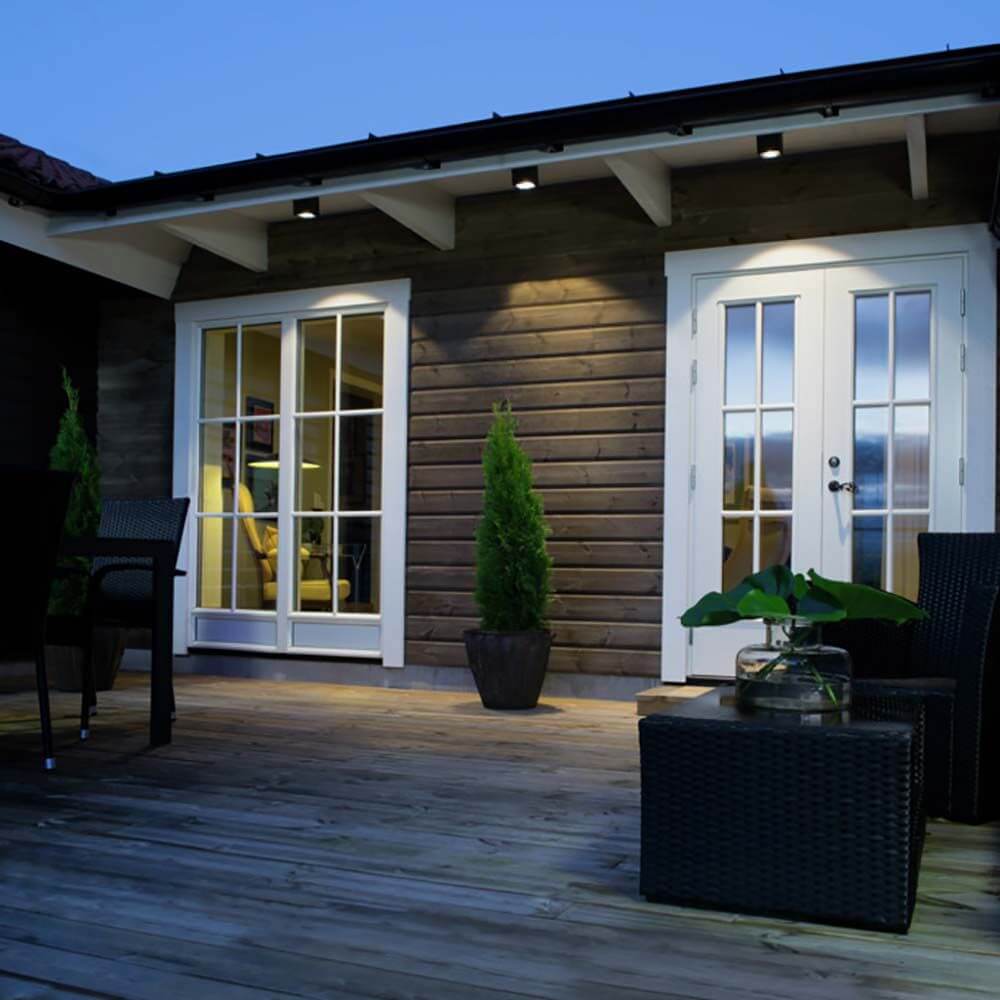 Cesena LED Außen Deckenaufbauleuchte auf einer Terrasse mit Holzdecke und Pflanzen.